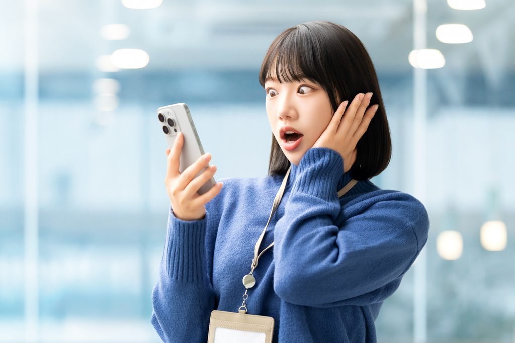 画像 スマホを見て驚く若い女性のビジネスパーソン